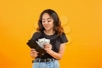 Asian woman putting money into wallet on color background�