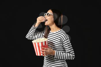 Young woman eating popcorn on dark background�