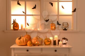 Halloween pumpkins and candles on table near window�