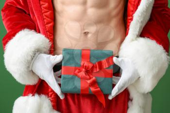 Young athletic Santa Claus with gift on color background, closeup�