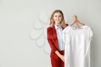 Female worker of modern dry-cleaner with clothes on light background�