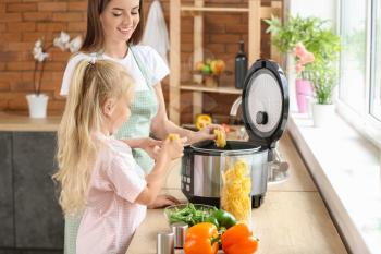 Woman and her little daughter using modern multi cooker in kitchen�
