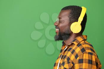 Handsome African-American man listening to music on color background�