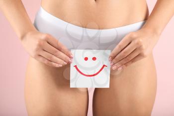 Young woman holding paper with drawn happy emotion on color background. Gynecology concept�