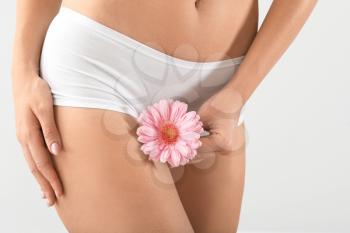 Young woman with flower on grey background, closeup. Gynecology concept�
