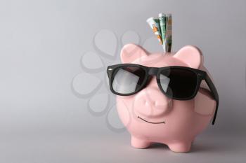 Piggy bank with sunglasses and money on grey background�