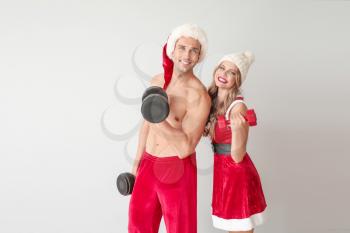 Young couple dressed as Santa Claus with dumbbells on light background�