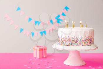 Tasty Birthday cake with gift on table against grey background�