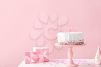 Tasty Birthday cake with gifts on table against color background�