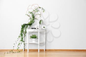Dressing table with green houseplants near white wall�