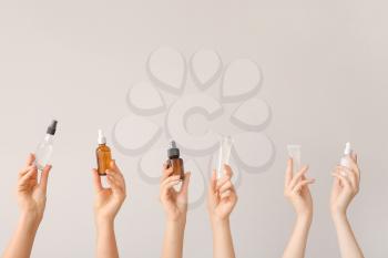 Female hands with different cosmetic products in bottles on grey background�