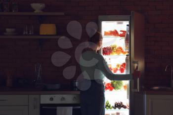 Young woman choosing food in refrigerator at night�