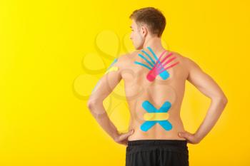 Sporty man with physio tape applied on back against color background�