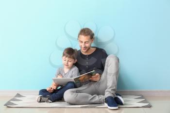 Father and his little son reading book near light wall�