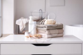 Stack of towels, cosmetics, loofah and brushes on table in bathroom�