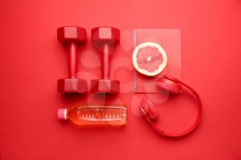 Dumbbells with notebook, headphones grapefruit and bottle of water on color background�
