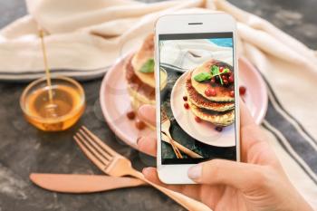 Female food photographer with mobile phone taking picture of pancakes�
