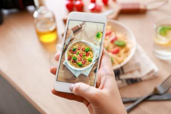 Female food photographer with mobile phone taking picture of pasta�