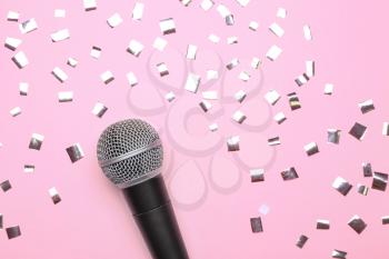 Modern microphone and confetti on color background�