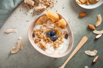 Tasty granola with yogurt in bowl on color background�