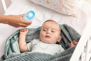 Mother with modern baby monitor near bed with sleeping child�