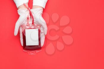 Hands of doctor with blood pack for transfusion on color background�