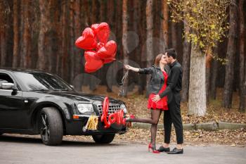 Happy young couple with air balloons near car outdoors. Valentine's Day celebration�