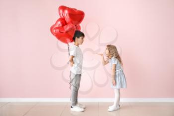 Little girl sending kiss for cute boy with air balloons on color background. Valentines Day celebration�