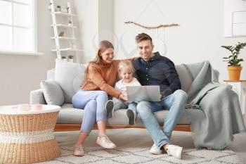 Happy young family with laptop sitting on sofa at home�