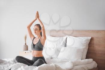 Beautiful young woman practicing yoga in bedroom�