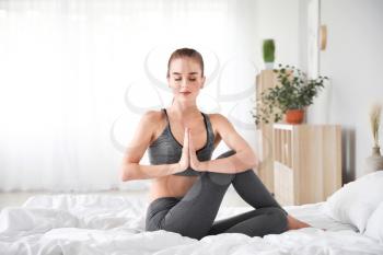 Beautiful young woman practicing yoga in bedroom�