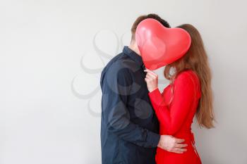 Happy young couple with heart-shaped balloon on light background. Valentine's Day celebration�