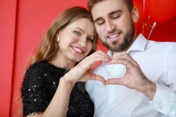 Happy young couple making heart with their hands on color background. Valentine's Day celebration�
