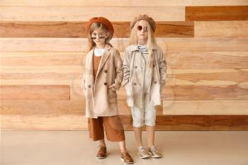 Cute little girls in autumn clothes near wooden wall�