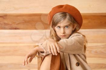 Cute little girl in autumn clothes sitting near wooden wall�