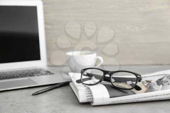 Newspaper, laptop and glasses on table�