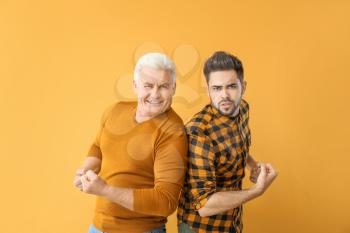 Young man and his father showing biceps on color background�