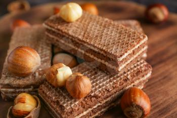 Tasty chocolate waffles with hazelnuts on wooden board, closeup�