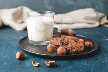 Tasty chocolate cookies with hazelnuts and glass of milk on dark background�