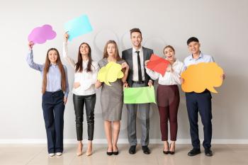Group of business people with blank speech bubbles near light wall�