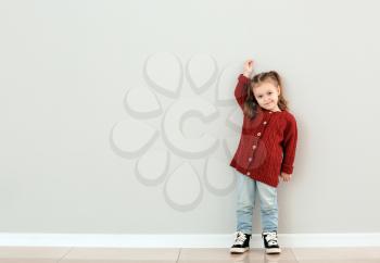 Cute little girl measuring height near grey wall�