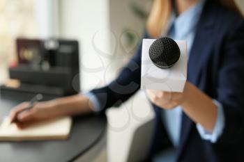 Female journalist with microphone having an interview in office, closeup�