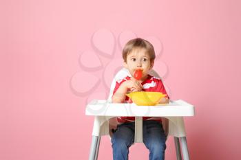 Cute little boy eating tasty baby food against color background�