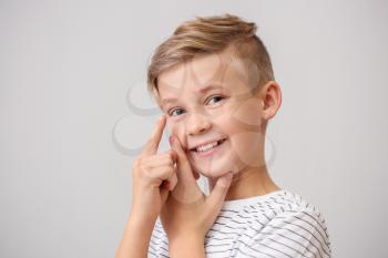 Little boy putting in contact lens on grey background�