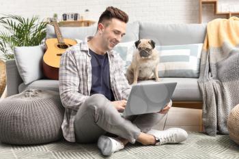 Handsome man with laptop and cute pug dog at home�