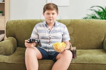 Overweight boy with chips playing video game at home�