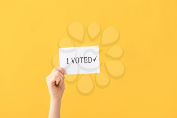 Hand holding paper with text I VOTED on color background�