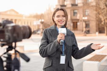 Beautiful journalist with microphone outdoors�