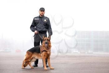 Male police officer with dog patrolling city street�