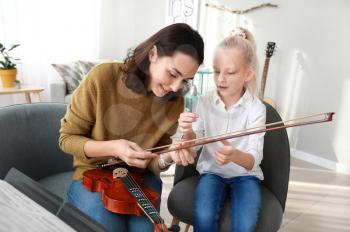 Private music teacher giving violin lessons to little girl at home�
